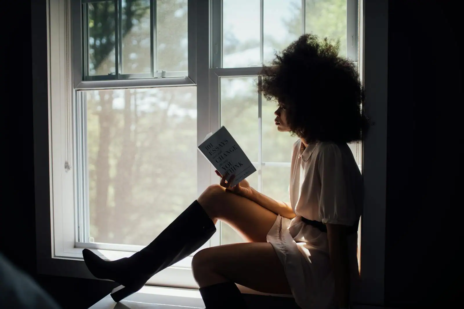Femme installée près d'une fenêtre, lisant calmement un livre de développement personnel