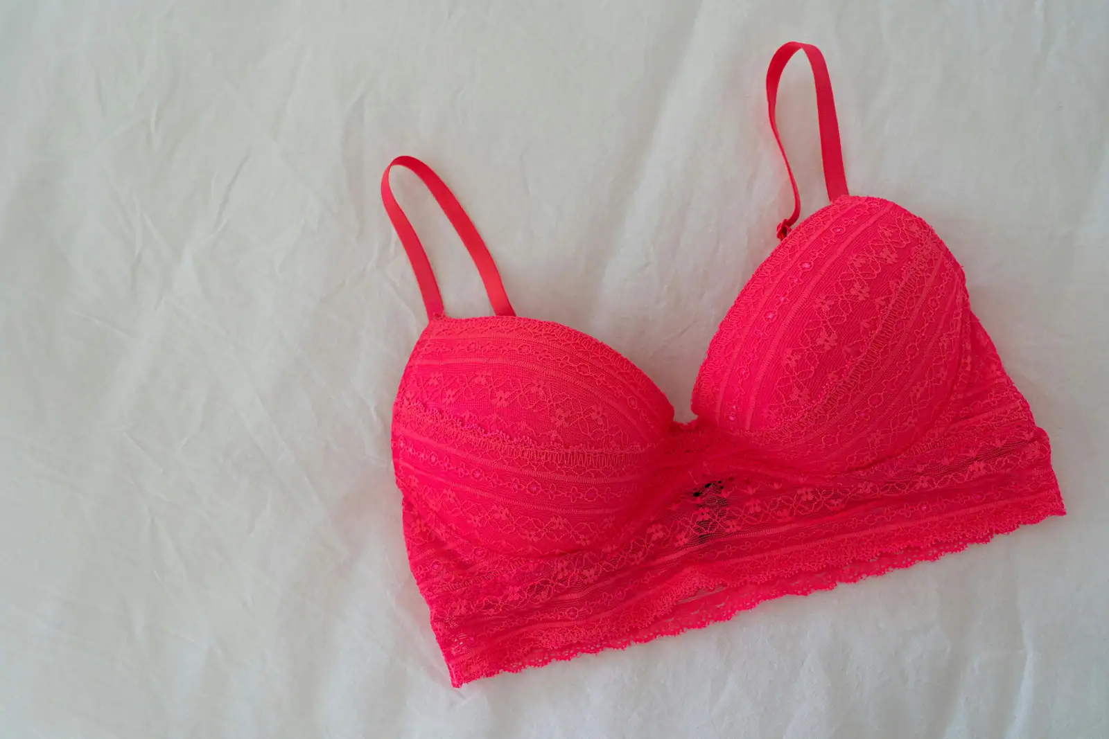 Soutien-gorge en dentelle rose posé à plat sur un drap clair, avec ses bretelles réglables visibles.