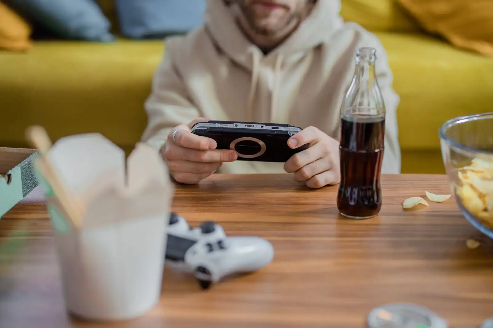 Un joueur tient une console de jeu portable à table, une manette posée à côté.