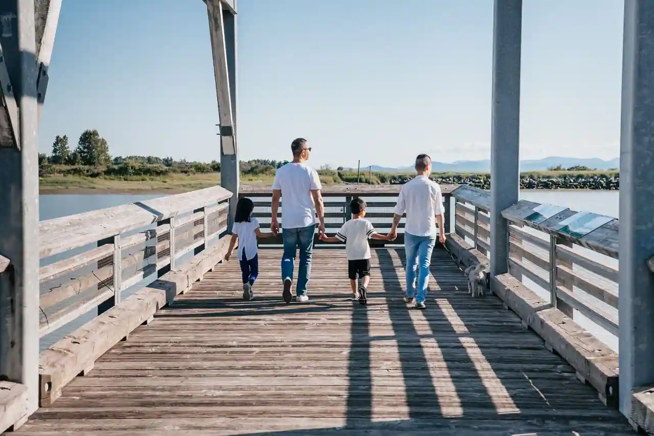 Famille avec deux enfants marchant de dos sur un ponton en bois au bord de l'eau par beau temps.