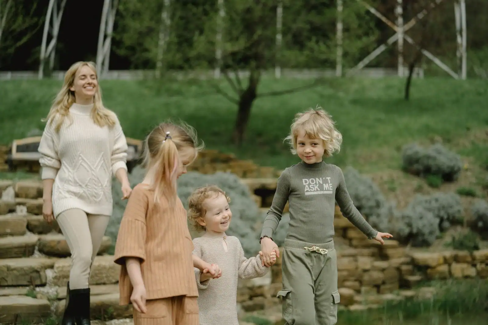 Mère et trois enfants se promenant main dans la main dans un parc verdoyant