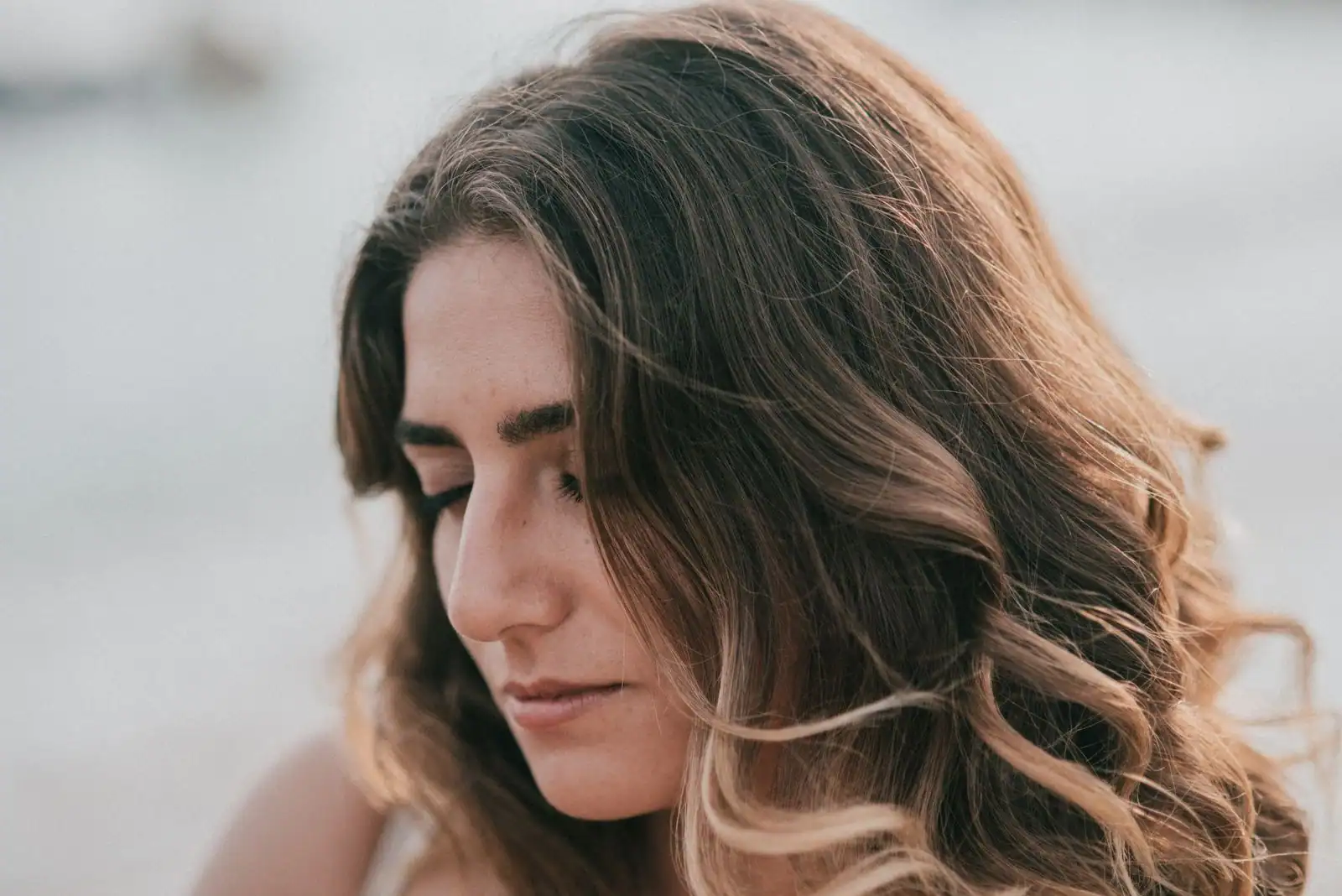 Femme aux cheveux blond foncé ondulés aux reflets miel, de profil en lumière naturelle.