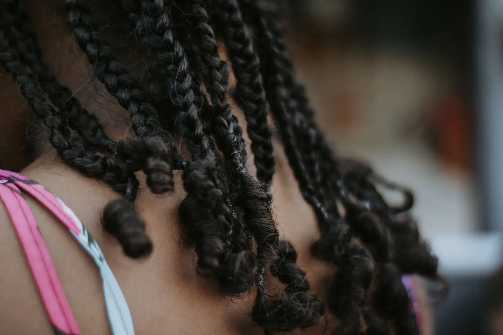 Gros plan sur la nuque d'une femme aux cheveux crépus coiffés en fines tresses aux pointes bouclées.