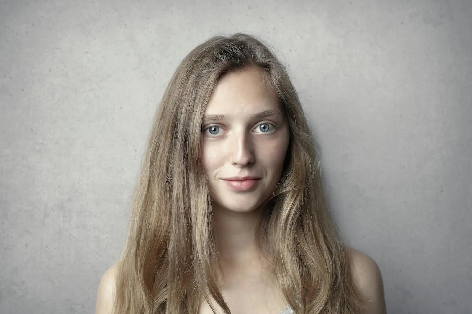 Jeune femme aux longs cheveux blonds, portrait sur fond gris clair.