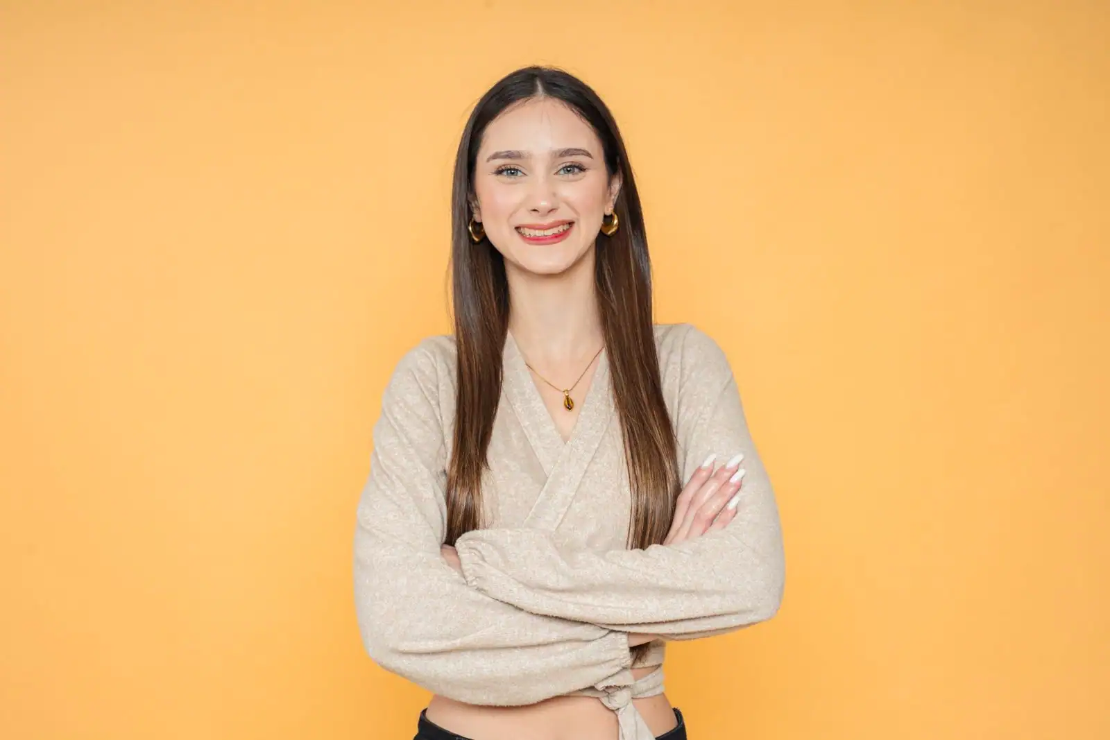 Jeune femme souriante, bras croisés et posture assurée sur fond orange uni.