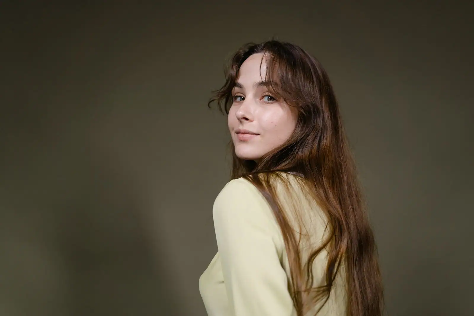 Femme brune aux longs cheveux ondulés avec frange rideau, coiffés en mouvement, vue de trois quarts.