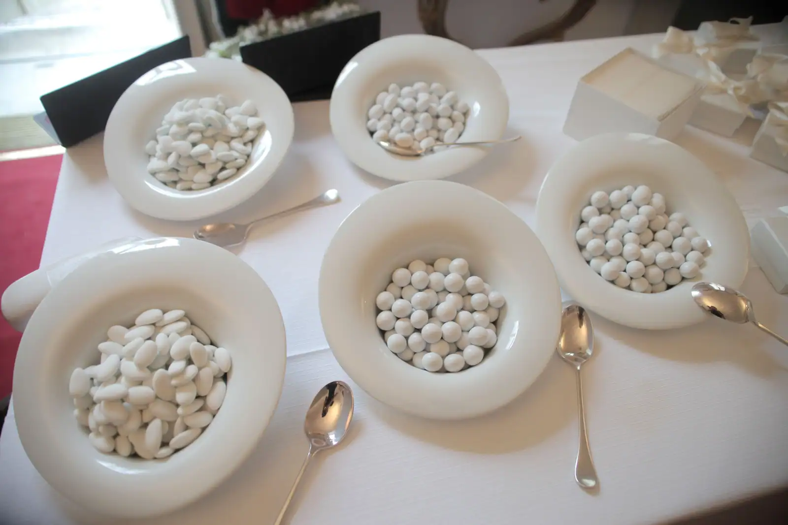 Dragées blanches présentées dans des coupelles blanches avec des cuillères, sur une table de réception