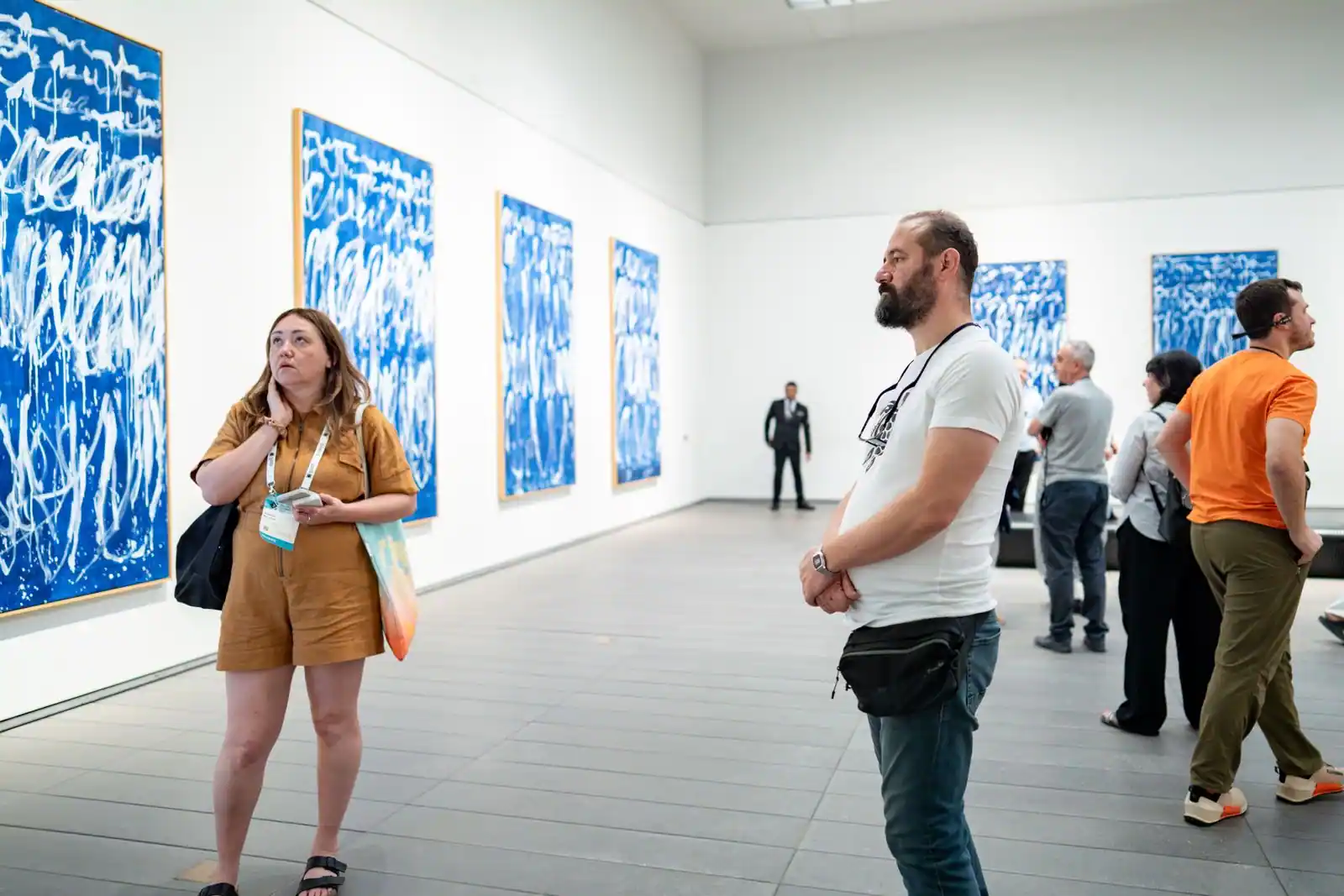 Des visiteurs observent des tableaux accrochés dans la galerie lumineuse d'un musée d'art.
