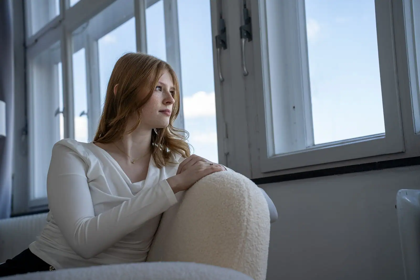 Jeune femme assise près d'une fenêtre, calme et pensive, baignée d'une lumière naturelle douce