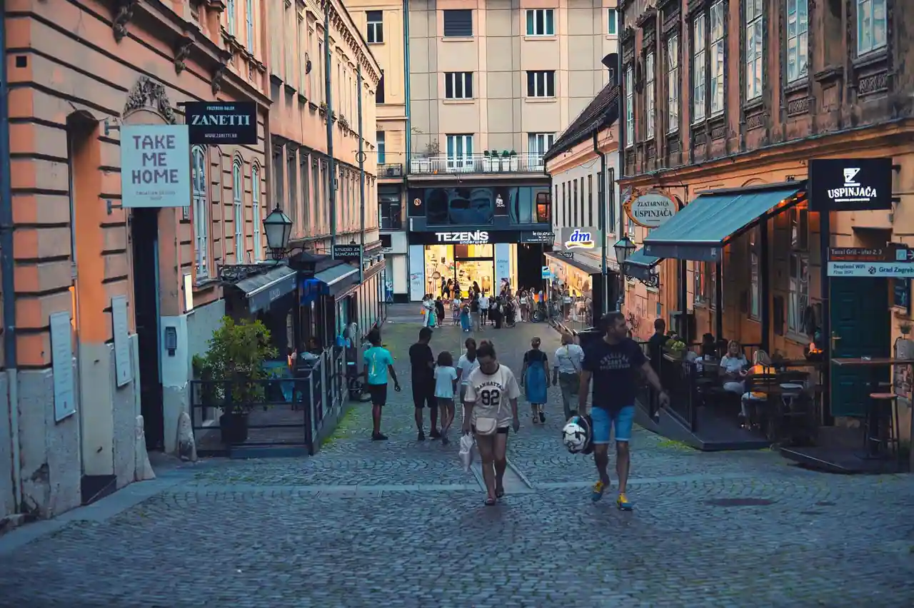 Rue pavée et piétonne animée d'une ville en fin de journée, passants, boutiques et terrasses de café