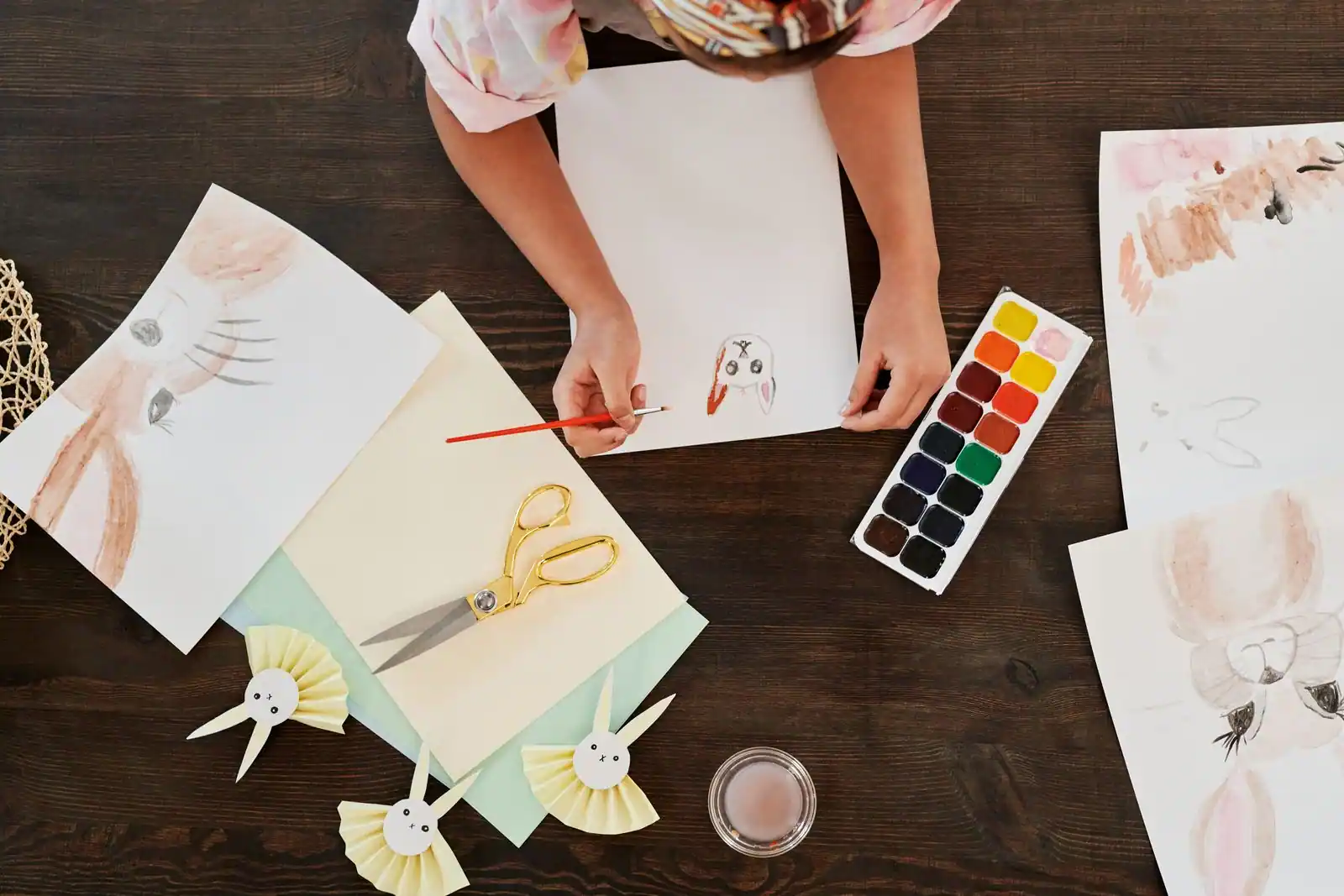 Une personne peint à l'aquarelle, entourée de fournitures de loisirs créatifs disposées sur une table