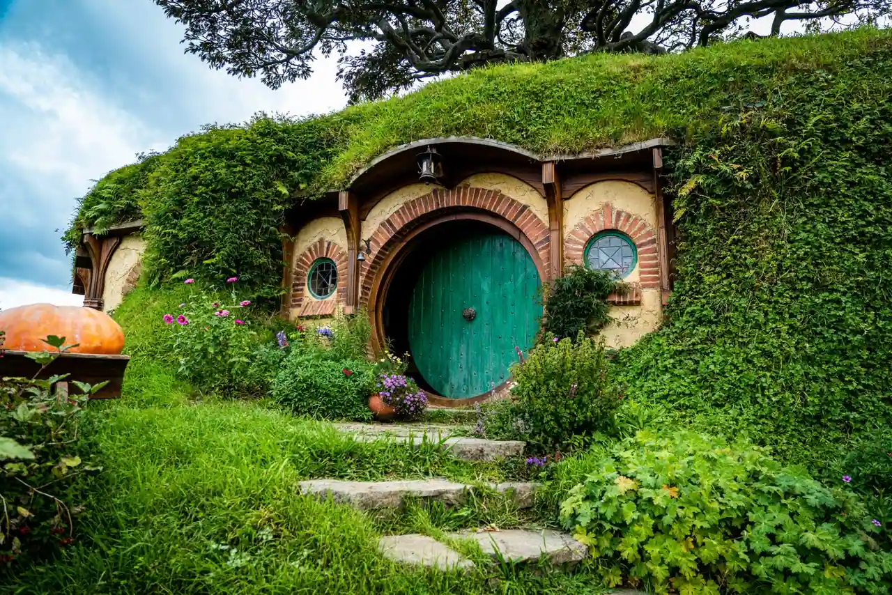 Maison de hobbit à la porte ronde verte, nichée dans une colline herbeuse au toit végétalisé