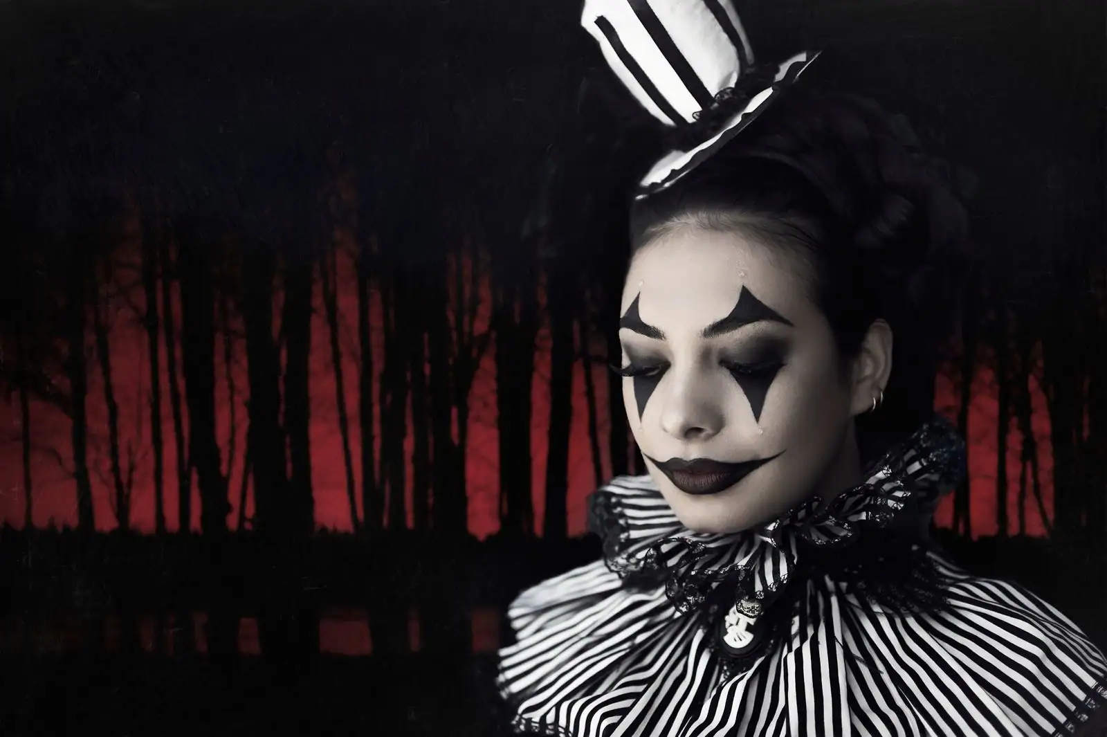 Maquillage de personnage théâtral : teint pâle, losanges noirs autour des yeux et bouche allongée.