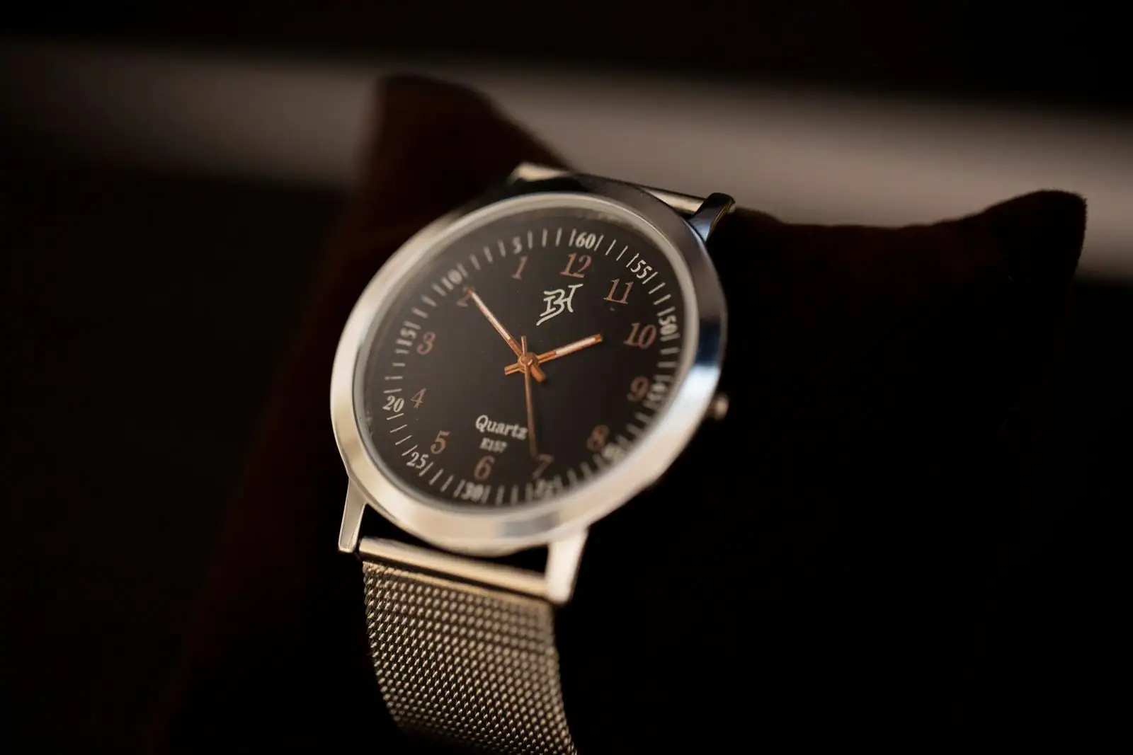 Montre à cadran rond noir et bracelet en maille métallique argentée, présentée sur un coussin