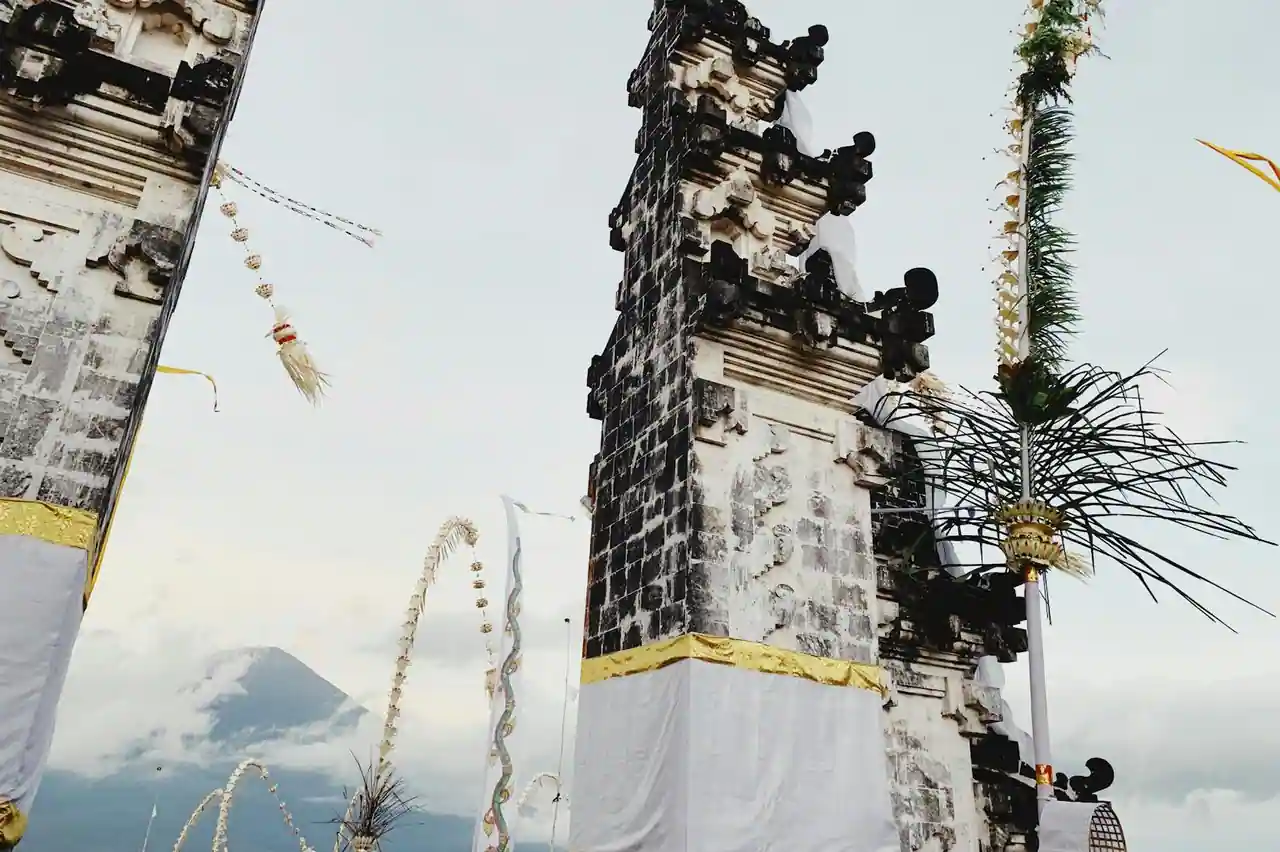 Temple hindou balinais en pierre volcanique avec porte fendue (candi bentar), décoré de tissus et de penjor, un volcan en arrière-plan.