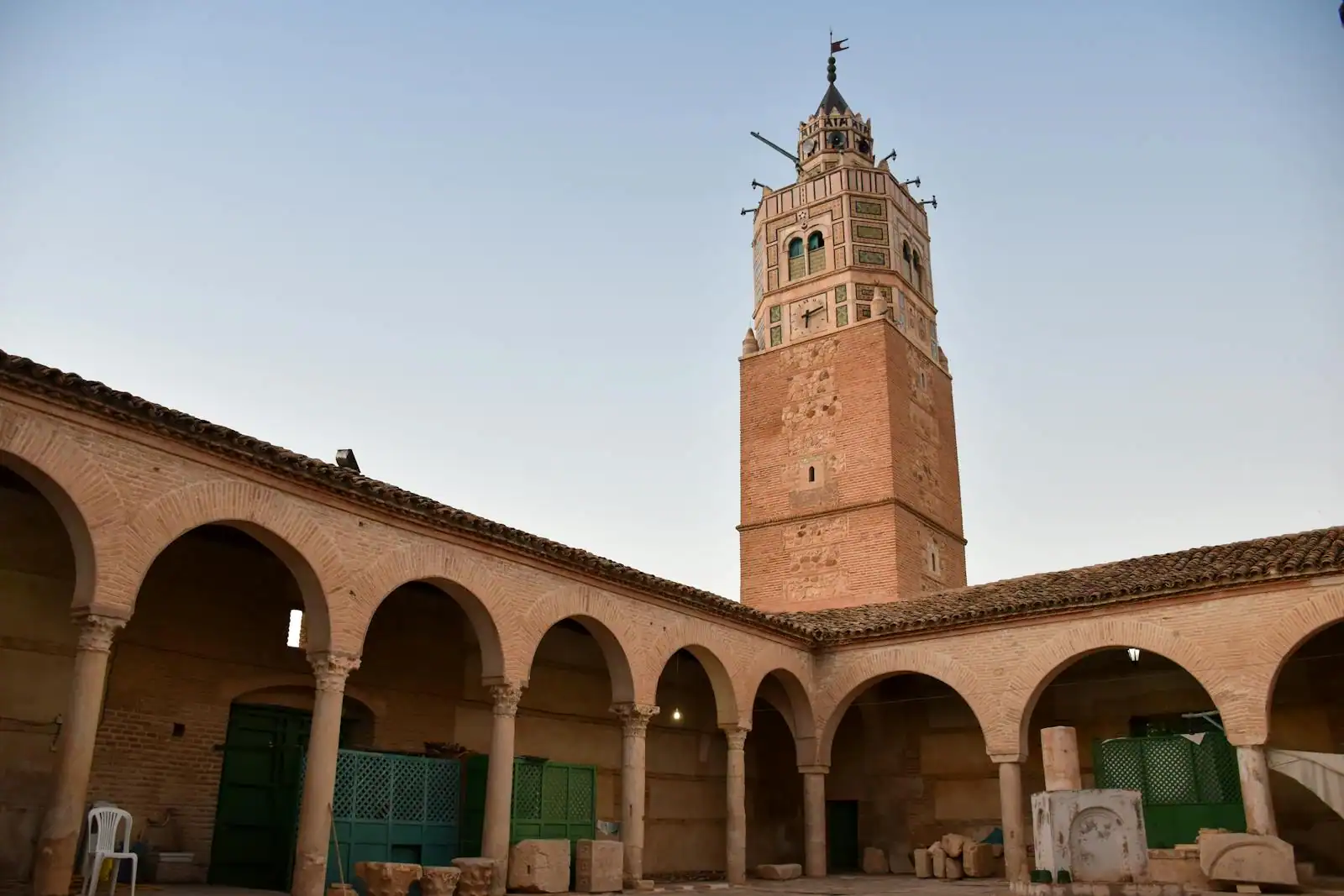 Cour intérieure d'une mosquée bordée d'arcades, dominée par un haut minaret de couleur ocre, sous un ciel clair