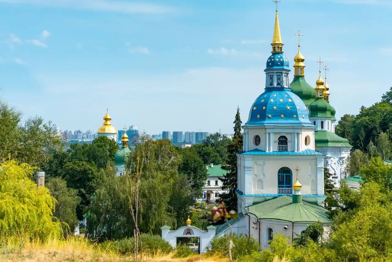 Église orthodoxe ukrainienne aux coupoles dorées et à la coupole bleue étoilée, sous un ciel clair.