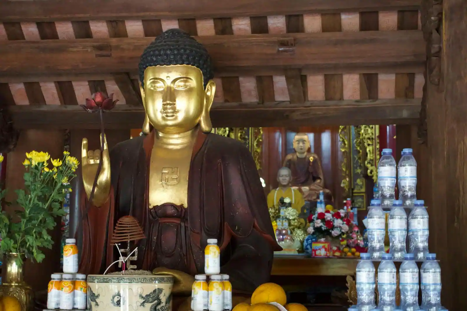 Statue de Bouddha doré dans une pagode vietnamienne, entourée d'offrandes de fleurs et de fruits