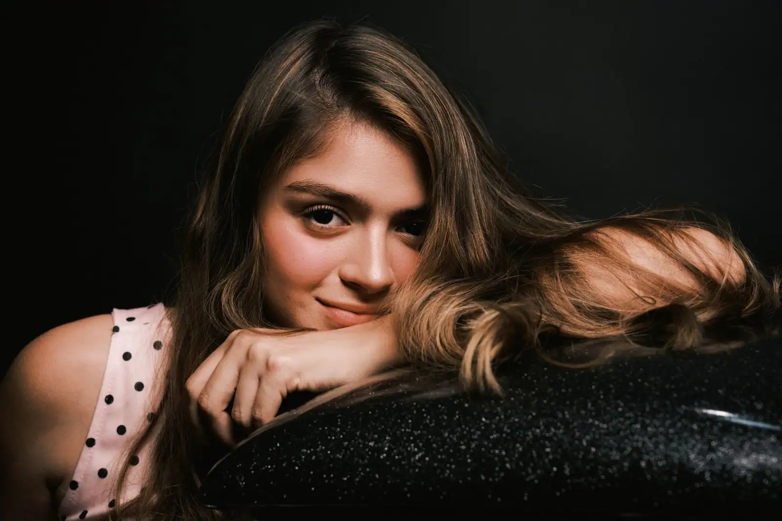 Portrait d'une jeune femme aux cheveux ondulés, au sourire doux et au regard charmeur, dans une lumière chaude et feutrée.
