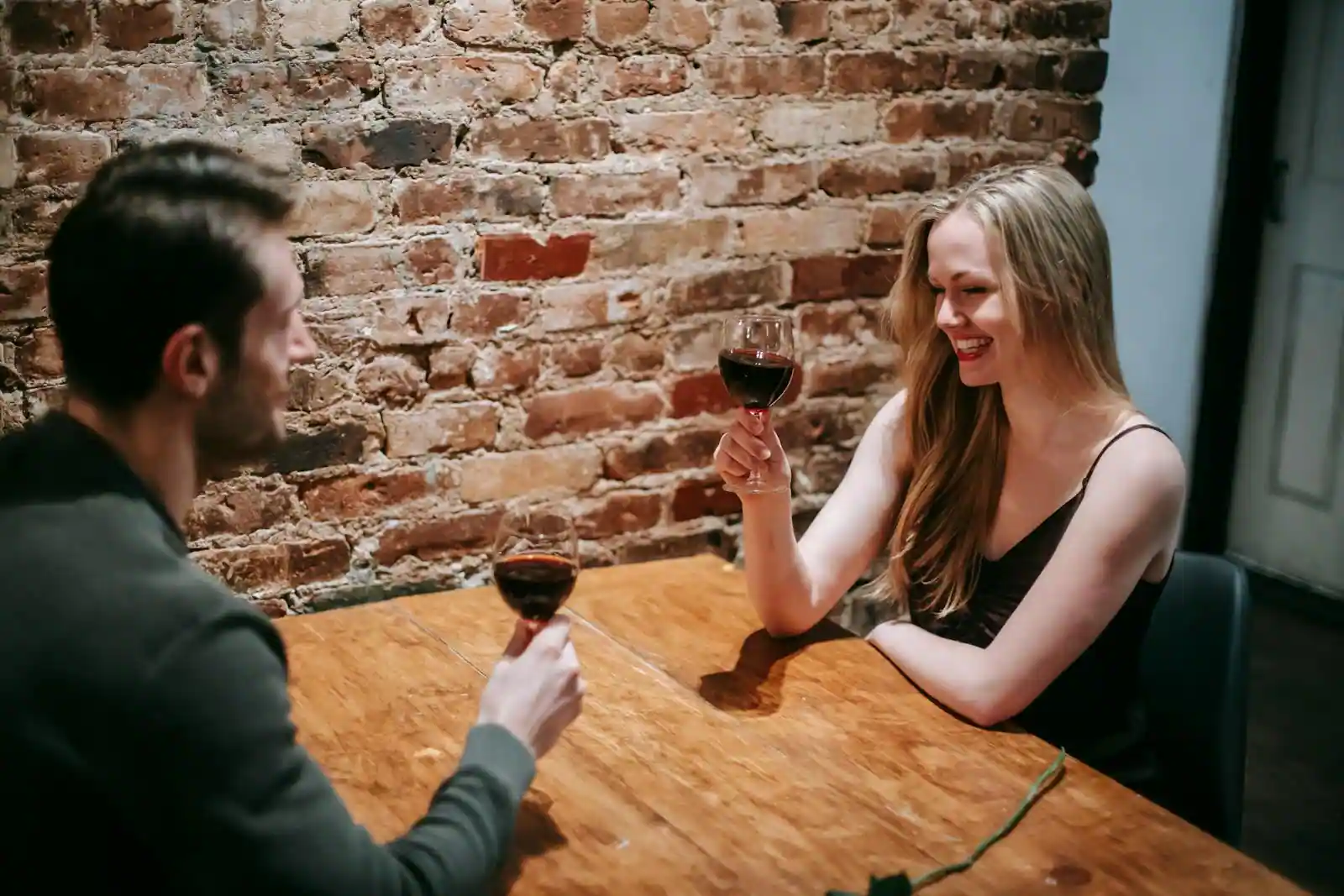 Un couple souriant lors d'un rendez-vous, partageant un verre de vin rouge à une table