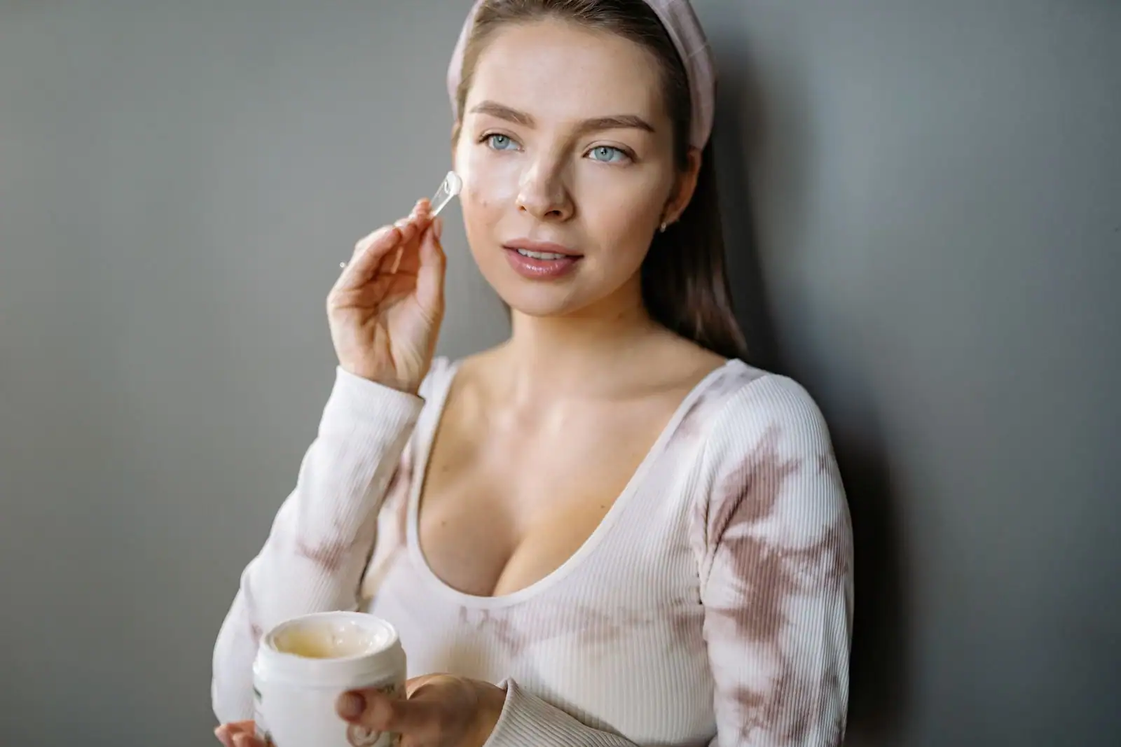 Jeune femme appliquant une crème de soin sur son visage, un pot de crème à la main