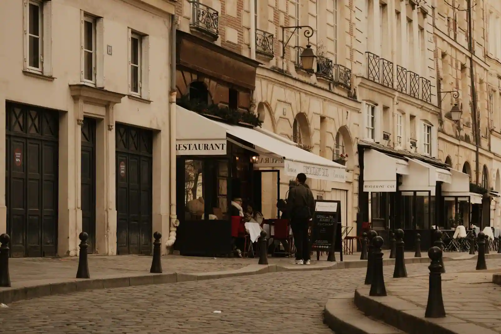 Terrasse de café et façades haussmanniennes dans une rue pavée de Paris.