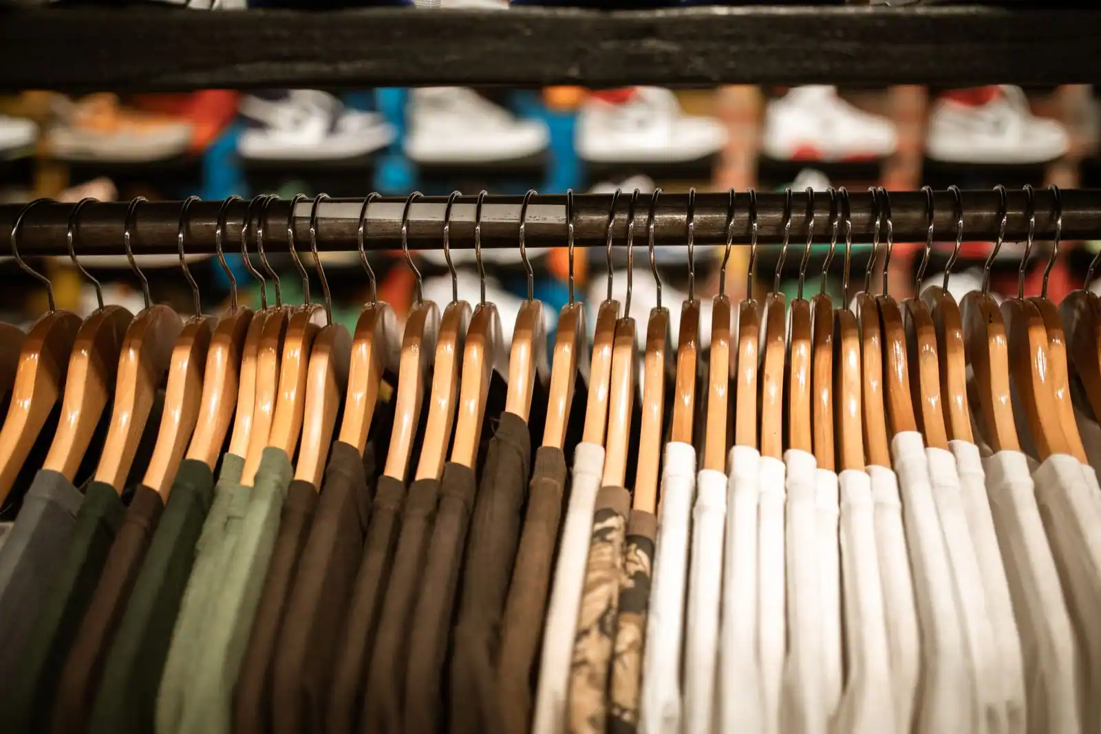 Des vêtements suspendus sur des cintres en bois, alignés sur un portant dans une boutique