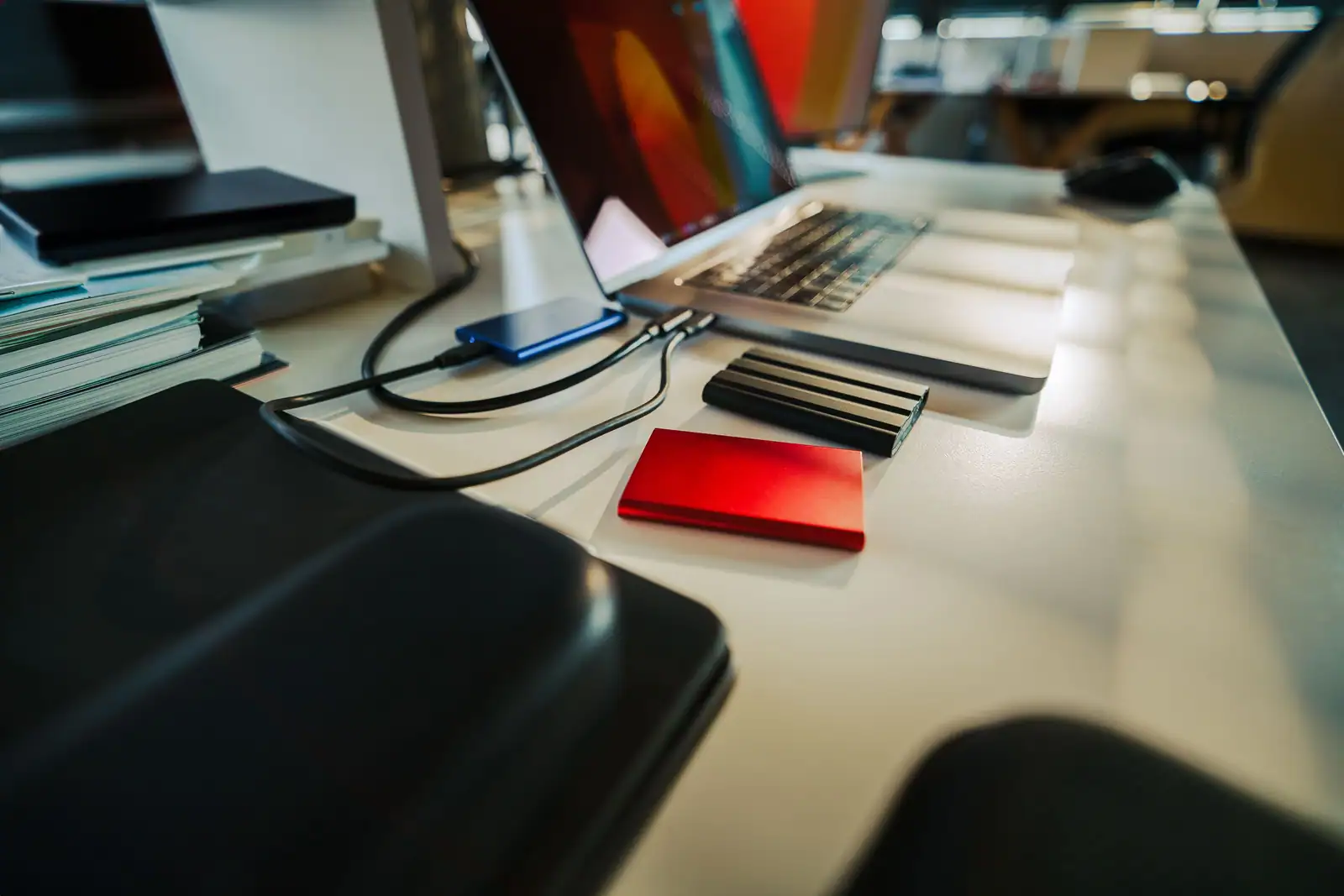 Ordinateur portable relié par câbles à plusieurs disques externes posés sur un bureau lumineux