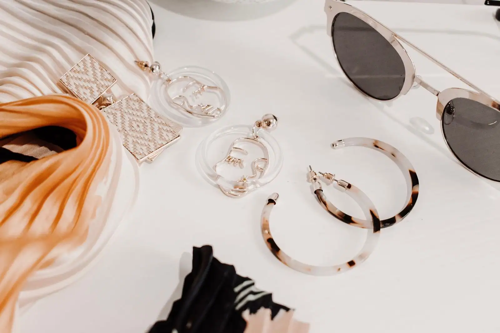 Accessoires de mode à plat sur fond clair : lunettes de soleil, boucles d'oreilles et foulard