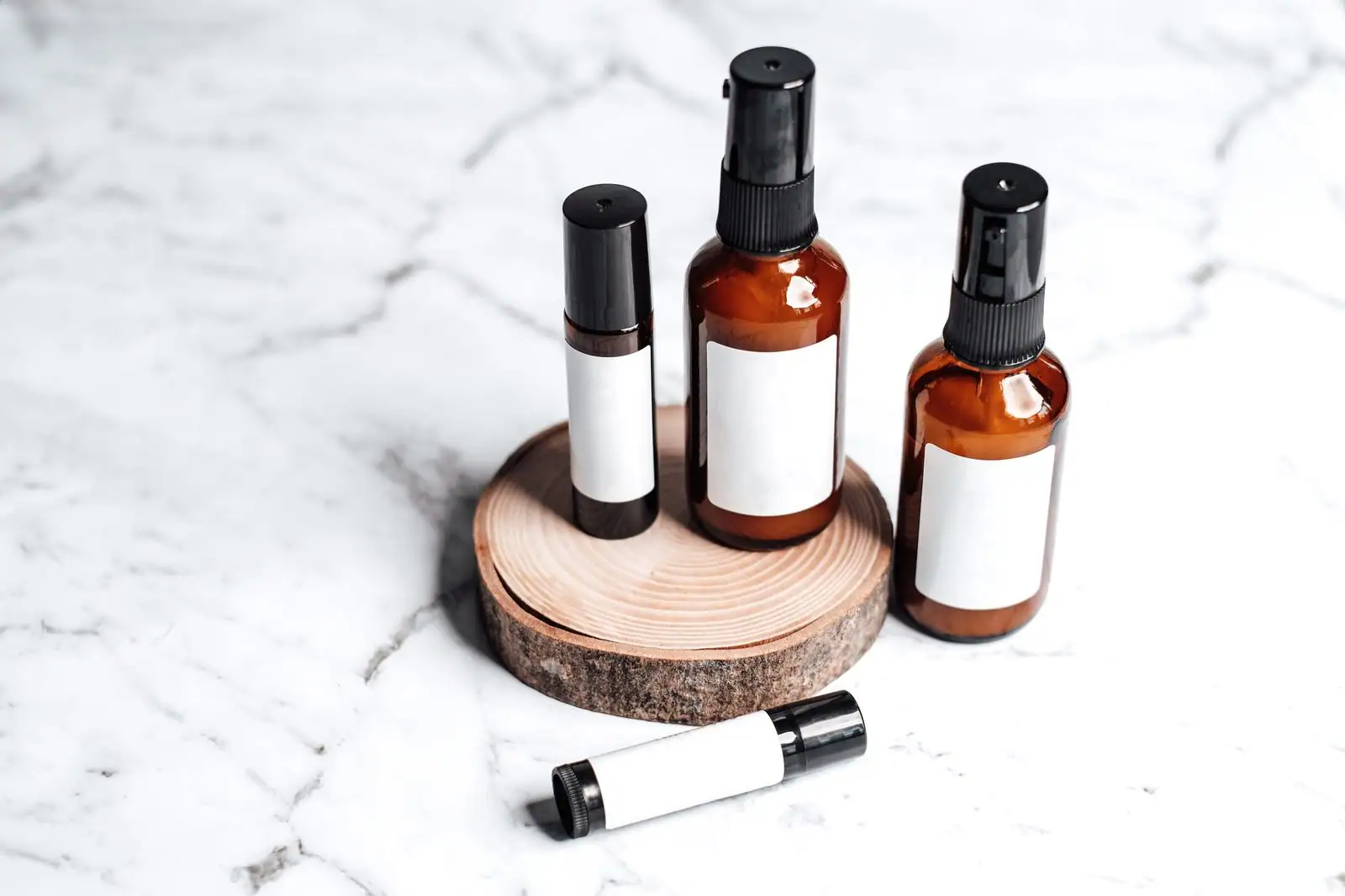 Flacons cosmétiques ambrés à étiquettes vierges posés sur un rondin de bois et un marbre blanc
