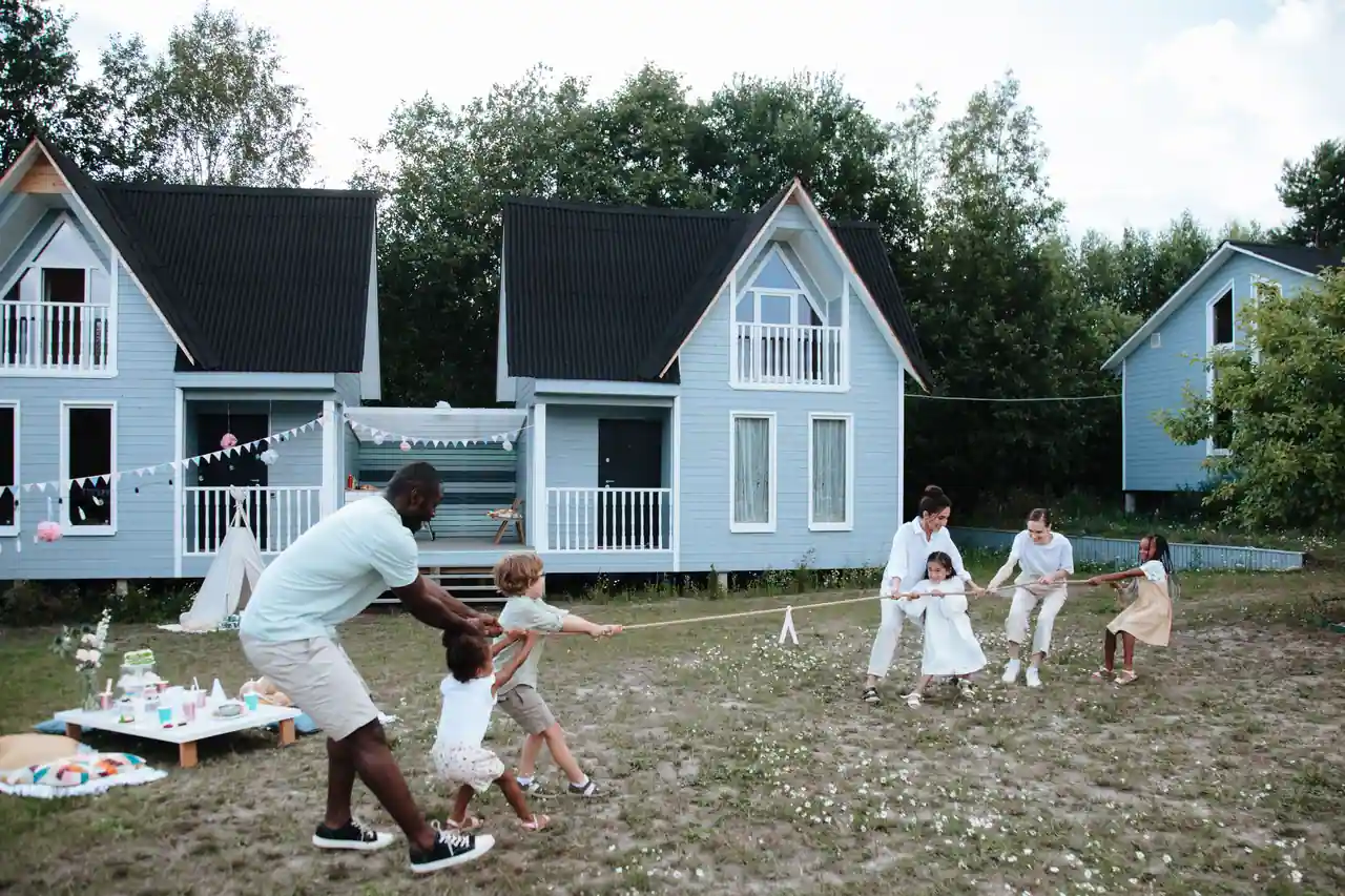 Adultes et enfants jouant ensemble en plein air devant des maisons, lors d'une activité entre familles