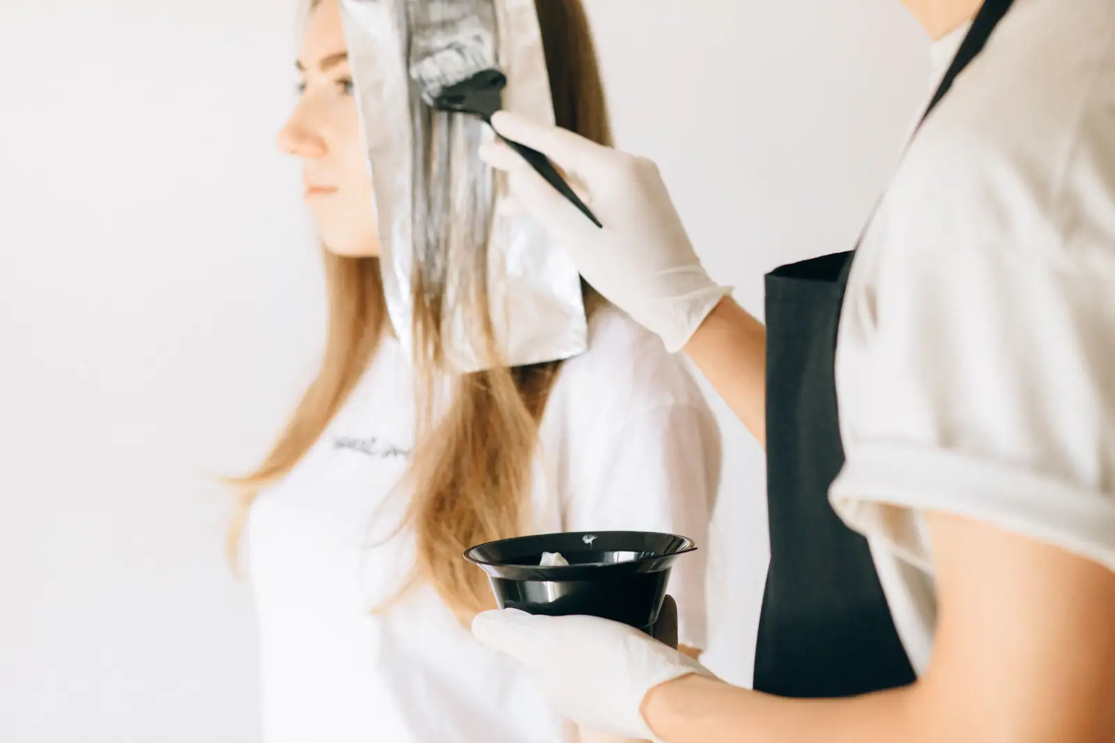 Coloriste appliquant la couleur au pinceau sur une mèche enveloppée d'aluminium, sur cheveux blonds