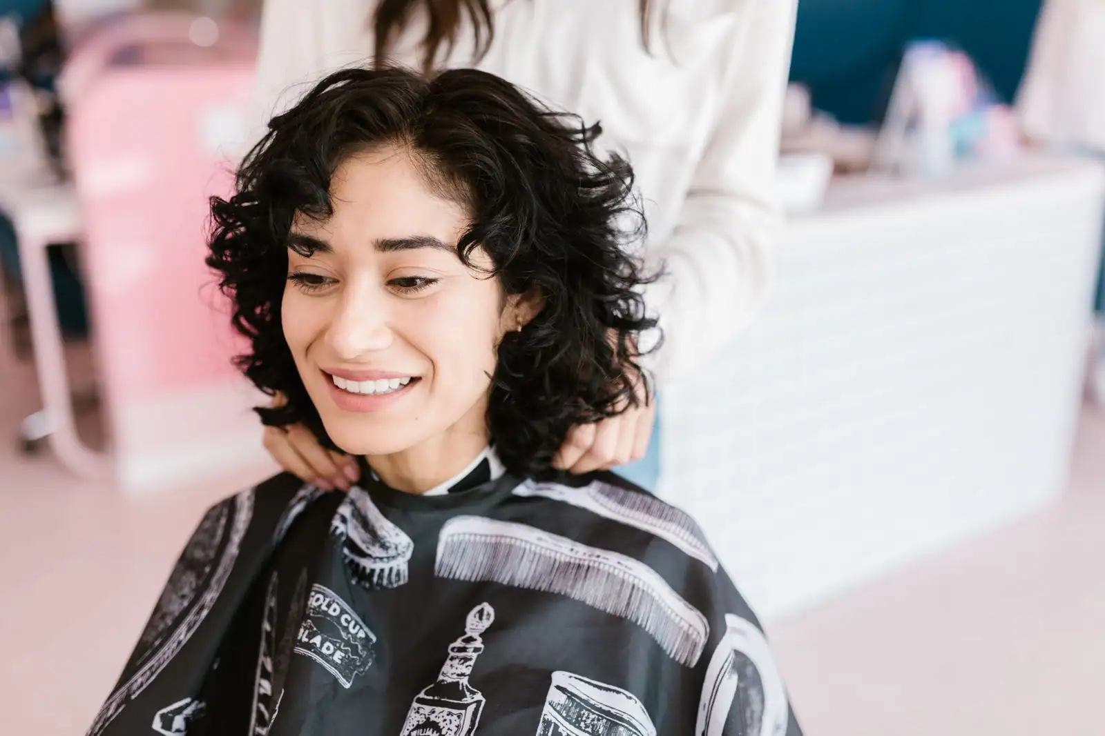 Femme aux cheveux bouclés mi-longs dans un salon de coiffure, cape de coupe sur les épaules