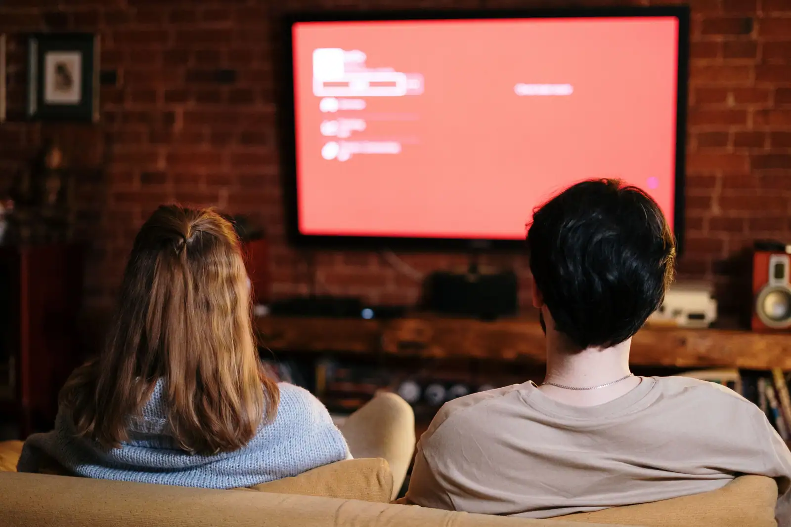 Deux personnes de dos devant un écran de télévision affichant un menu de programmes, le soir
