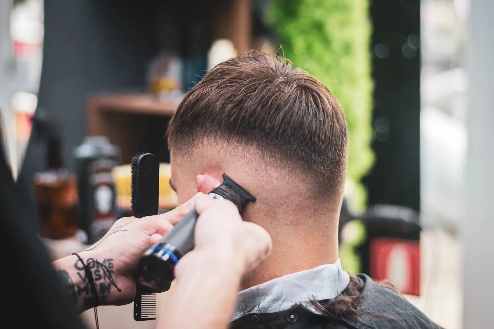 Coiffeur réalisant un dégradé à la tondeuse sur les cheveux d'un homme, en salon