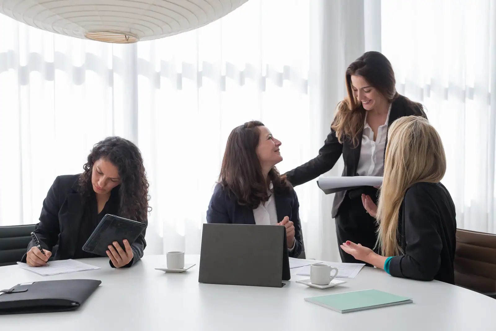 Réunion de travail entre quatre femmes en tailleur, l'une prend la parole, main ouverte, autour de la table