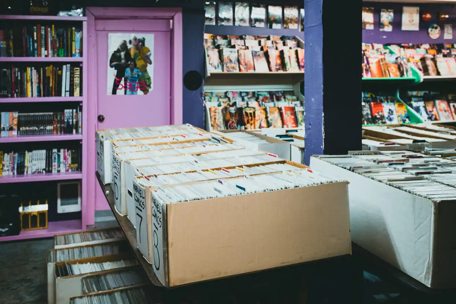 Bacs de comics d'occasion au premier plan et présentoirs de couvertures dans une boutique spécialisée.
