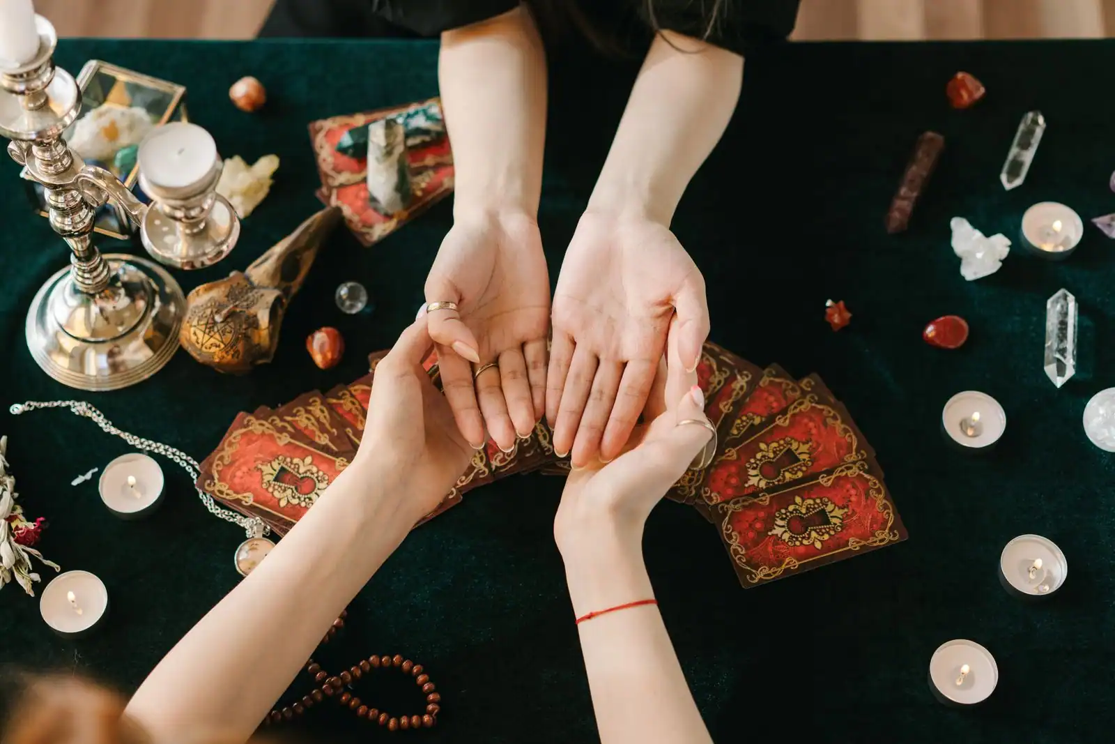 Mains jointes au-dessus d'un éventail de cartes de tarot, entourées de bougies et de pierres sur une table