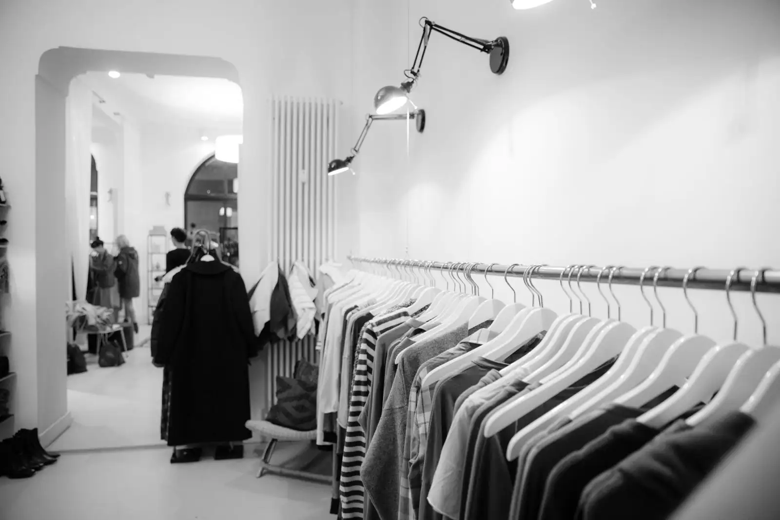 Intérieur en noir et blanc d'une boutique de vêtements indépendante, portants garnis et cliente de dos