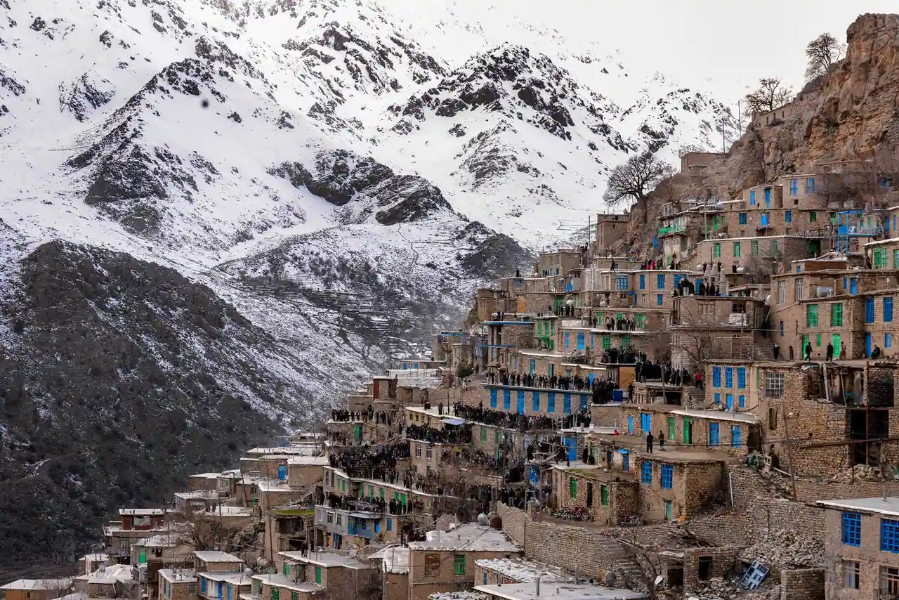 Village kurde aux maisons de pierre étagées à flanc de montagne, sous des sommets enneigés