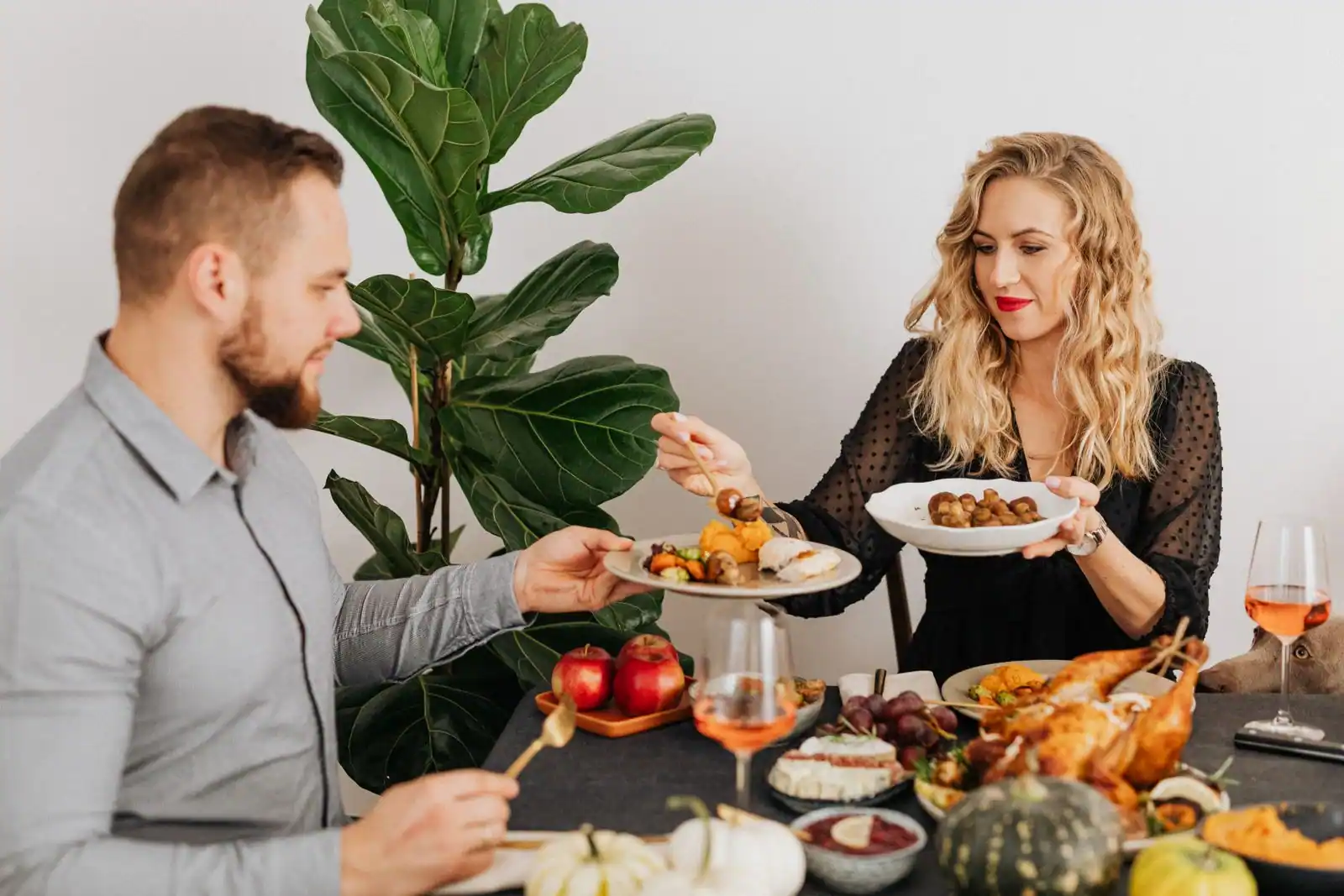 Une femme sert un plat dans l'assiette que lui tend un homme, autour d'une table garnie de mets partagés