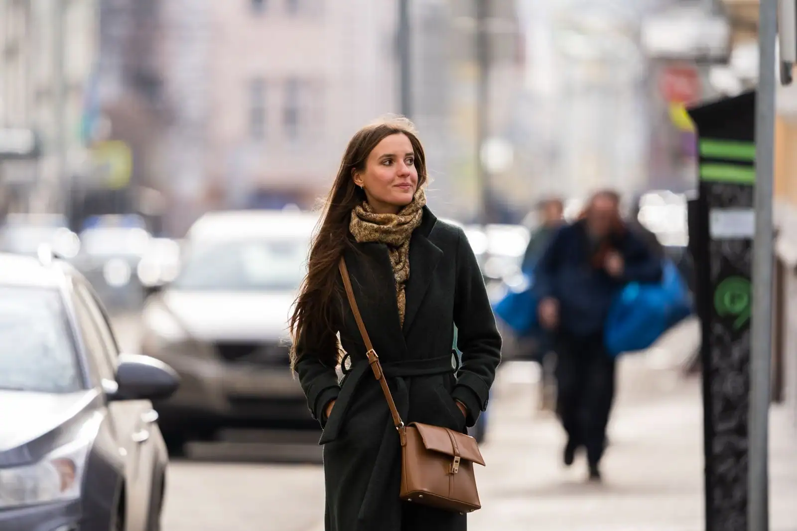 Femme en manteau long ceinturé à la taille et écharpe en grosse maille, dans une rue de ville