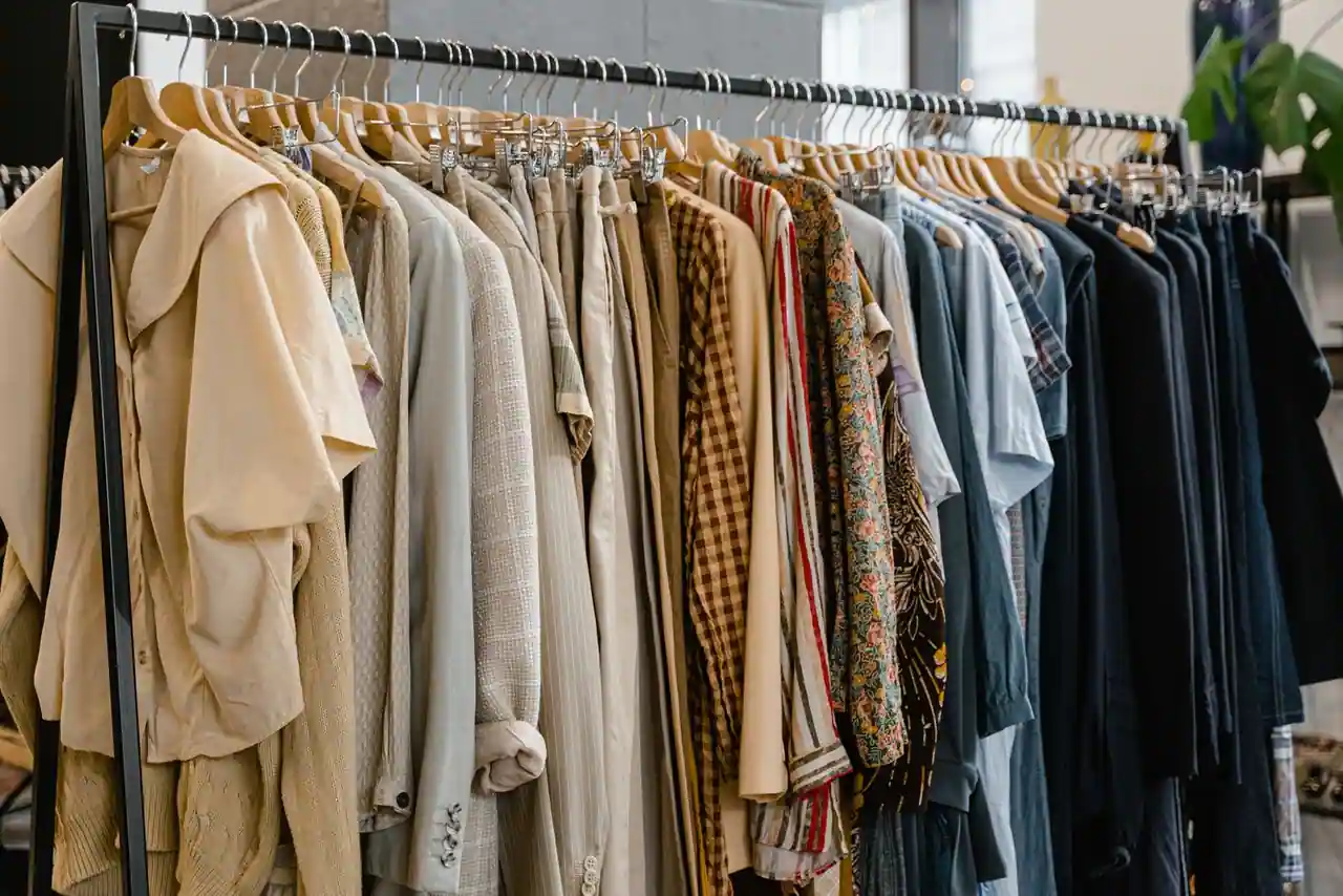 Portant de vêtements suspendus sur cintres, des pièces beiges aux vestes sombres, dans une pièce claire