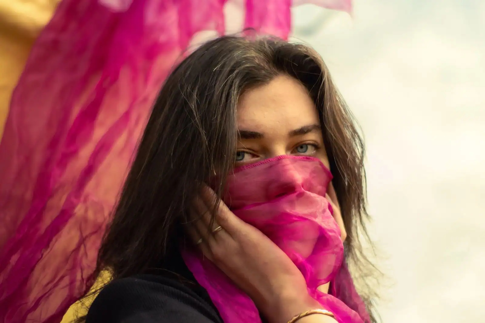 Jeune femme tenant un foulard en soie fuchsia devant son visage, bague fine à la main
