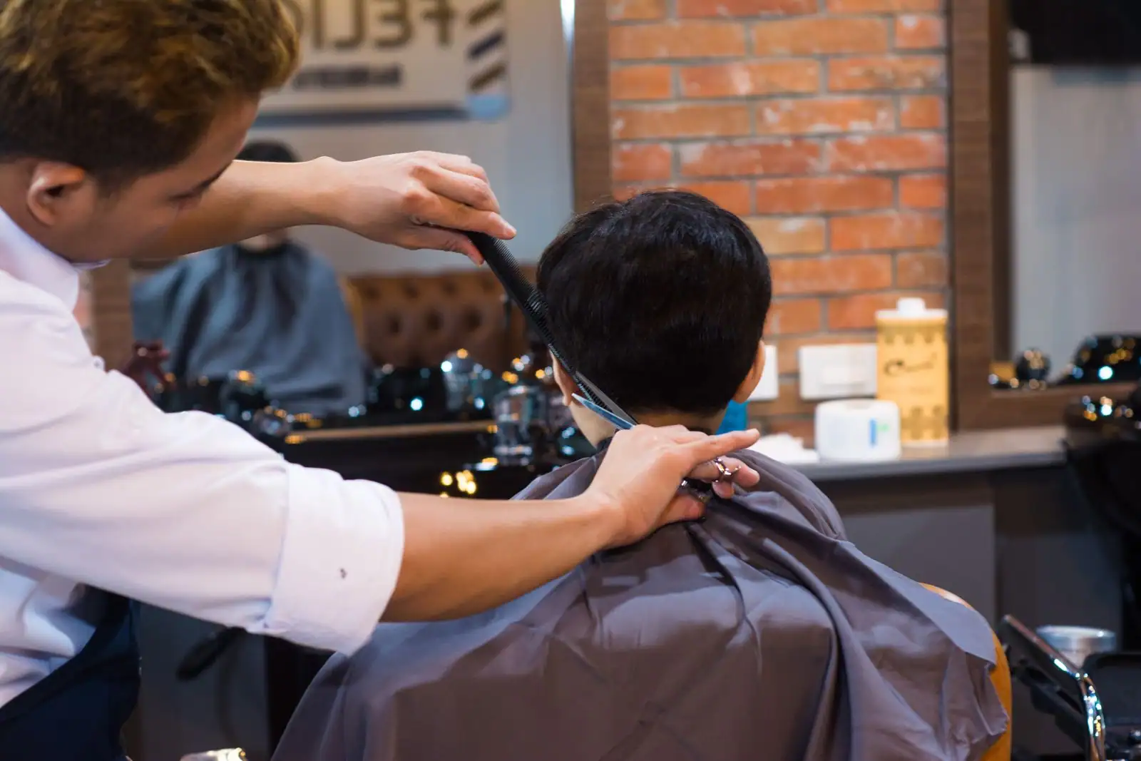 Un coiffeur ajuste un dégradé texturé sur un jeune homme assis dans un salon de coiffure