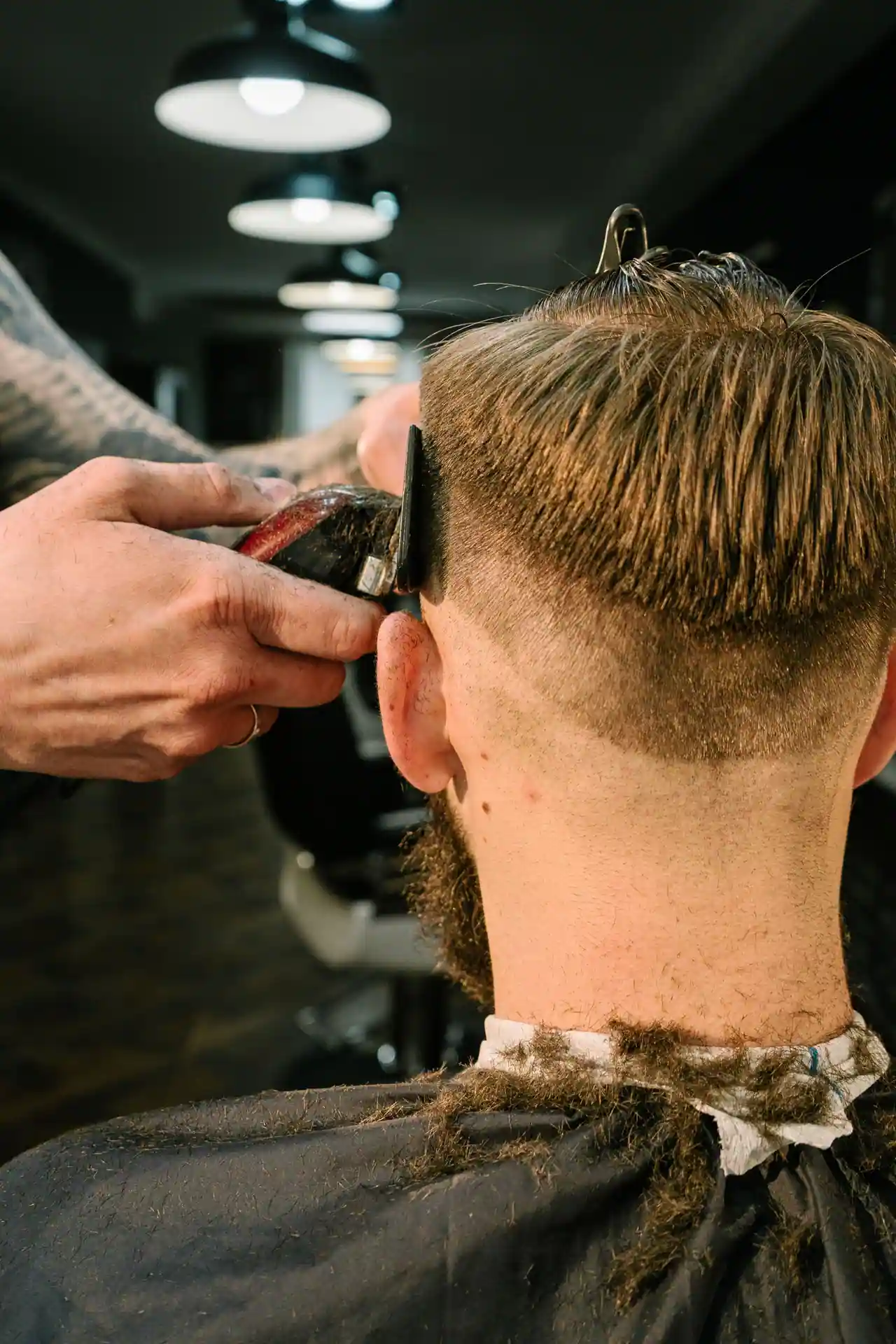 Barbier realisant un degrade taper fade aux tondeuses sur un client adulte, vue de dos.