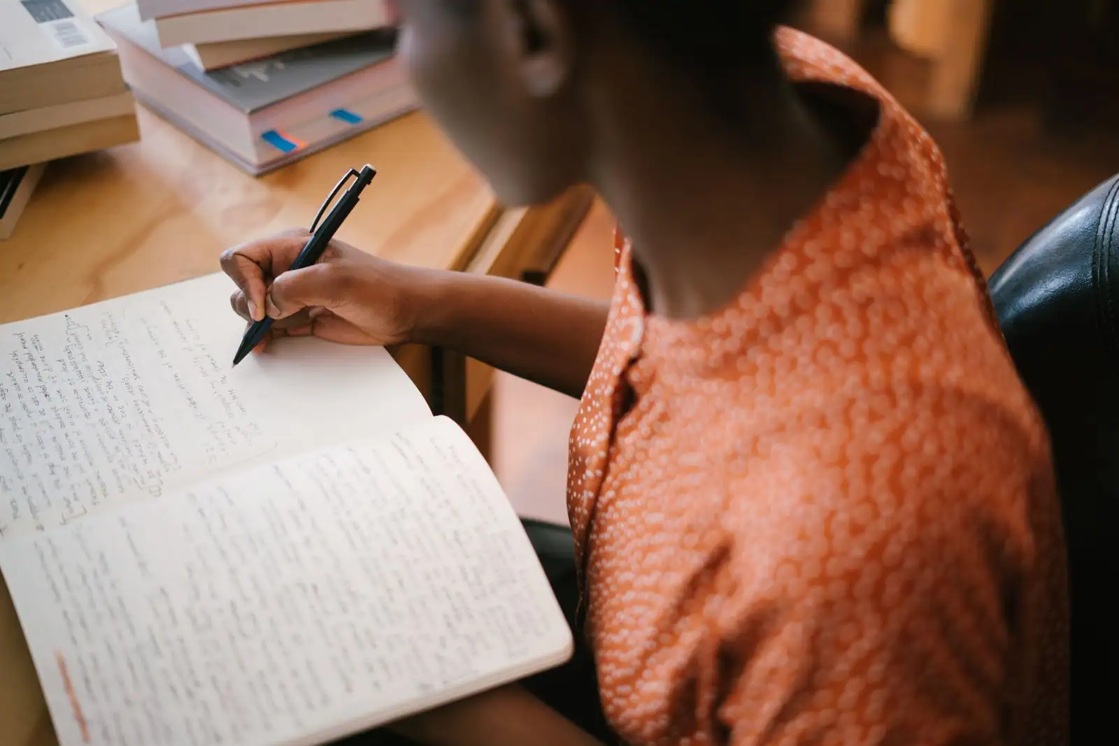 Personne écrivant dans un carnet, entourée de livres sur le développement personnel.