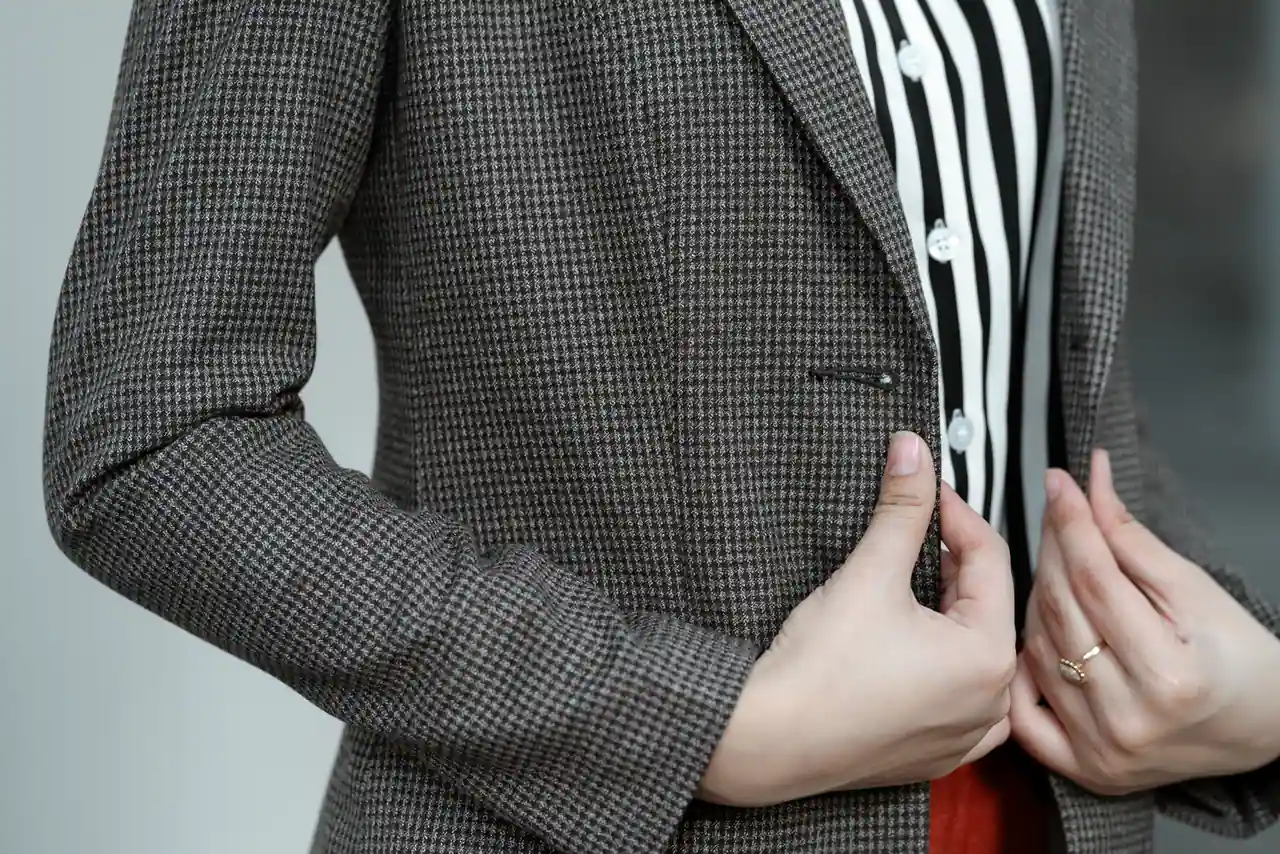 Gros plan sur un blazer à motif tweed porté sur une chemise rayée, main qui reboutonne la veste