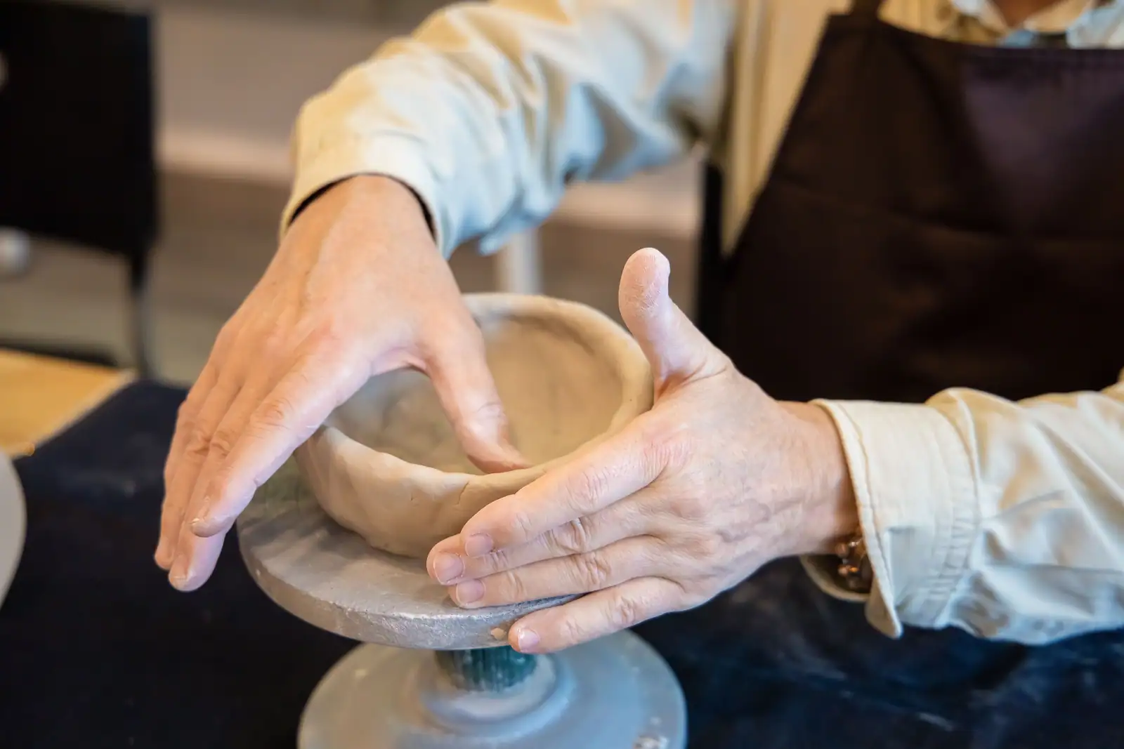Mains façonnant un petit bol en argile sur un tour de potier, lors d'un atelier de loisir créatif.
