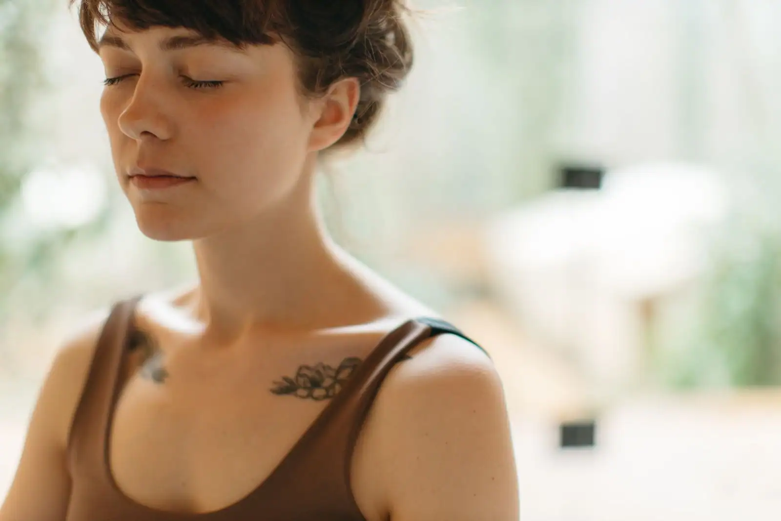 Une femme les yeux fermés, dans un moment de calme et de pleine conscience, en intérieur.